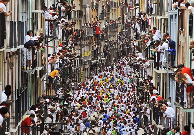 Runners make their way through the street with "El Pilar" fighting bulls watched by people from their balconies during the running of the bulls at the San Fermin festival, in Pamplona, Spain, Friday.