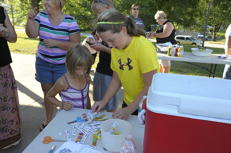 Macie Edwards, 10, from the Russellville Trinity Lutheran Church youth group helped guests, including Destiney Davis, 6, select water flavoring at the second of four community picnics, where children were sent home with bags of healthy snacks and hygiene products. News Tribune/Michelle Brooks