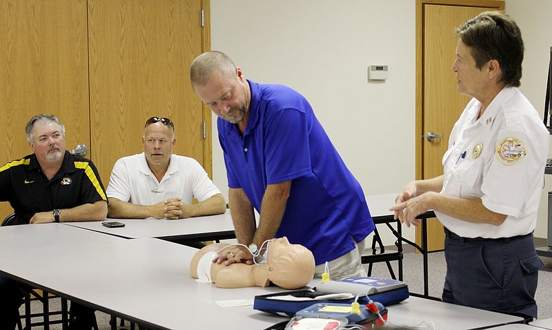 Kelly Drennan of the Callaway County Ambulance Service, right, demonstrates proper use of an automated external defibrillator (AED) to 12 Callaway County Courthouse employees during training Thursday morning. Applying CPR chest compressions is Don Horstman, Courthouse maintenance supervisor. In the background are, from left, Callaway County Eastern District Commissioner Randy Kleindienst and Presiding Commissioner Gary Jungermann.