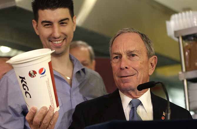 In this March 12, 2013 file photo, New York City Mayor Michael Bloomberg looks at a 64oz cup, as Lucky's Cafe owner Greg Anagnostopoulos, left, stands behind him. An appeals court ruled Tuesday, July 30, 2013 that New York City's Board of Health exceeded its legal authority and acted unconstitutionally when it tried to put a size limit on soft drinks served in city restaurants. 