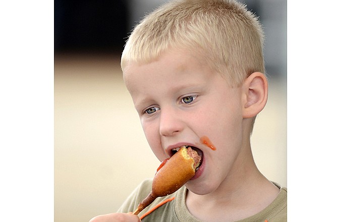 Nicholas Klinger, 5, of Jefferson City, enjoys a ketchup-covered corn dog with his family in front of the Jaycees food stand on Tuesday evening at the Jefferson City Jaycees Fair.
