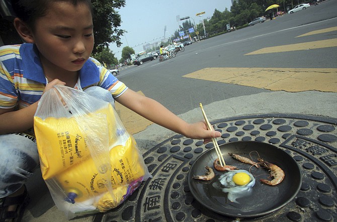 A child demonstrates Wednesday how raw shrimp and an egg are fried in a pan on a manhole cover on a hot summer day in Jinan in east China's Shandong province. A heat wave in China- the worst in at least 140 years in some parts - has left dozens of people dead and pushed thermometers above 104 degrees in at least 40 cities and counties, mostly in the south and east. 