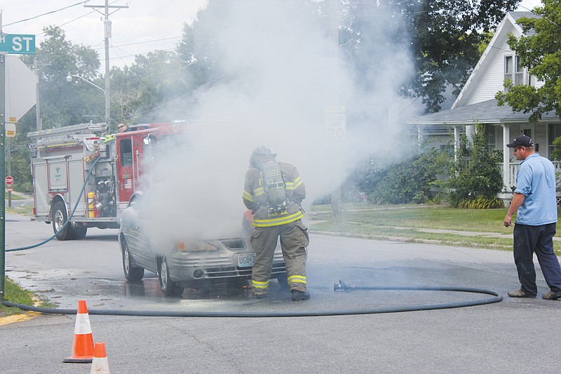 A Fulton firefighter begins to saw off the hood to a 1999 Pontiac Grand Am that's engine caught on fire Thursday at East 9th and Vine streets.