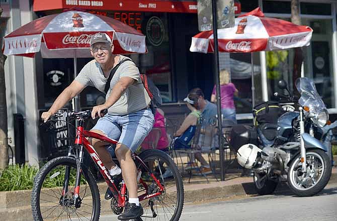 In this Aug. 24, 2013 photo, a man rides his bicycle down Jefferson City's High Street as others enjoy sitting at the outdoor tables and shopping.