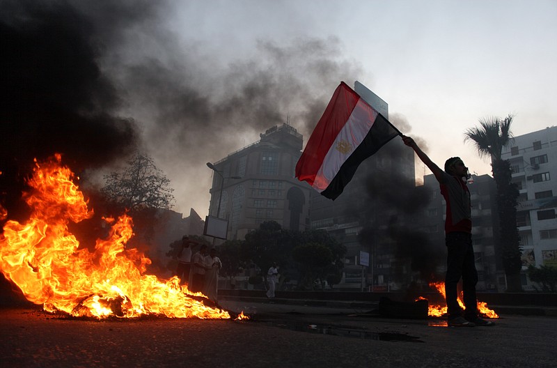 A supporter of Egypt's ousted President Mohammed Morsiv holds a national flag Friday as he stands next to burning tires during a protest in Cairo. Thousands of protesters and Muslim Brotherhood supporters rallied Friday throughout Egypt against a military coup and a bloody security crackdown.