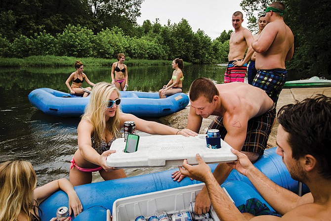 Jessica Keeven, left, and Jesse Marks, right, of Steelville, lift a cooler lid as Connor Mahurin reaches for a drink during a stop at a public access point for canoers and rafters on the Meramec River near Steelville.