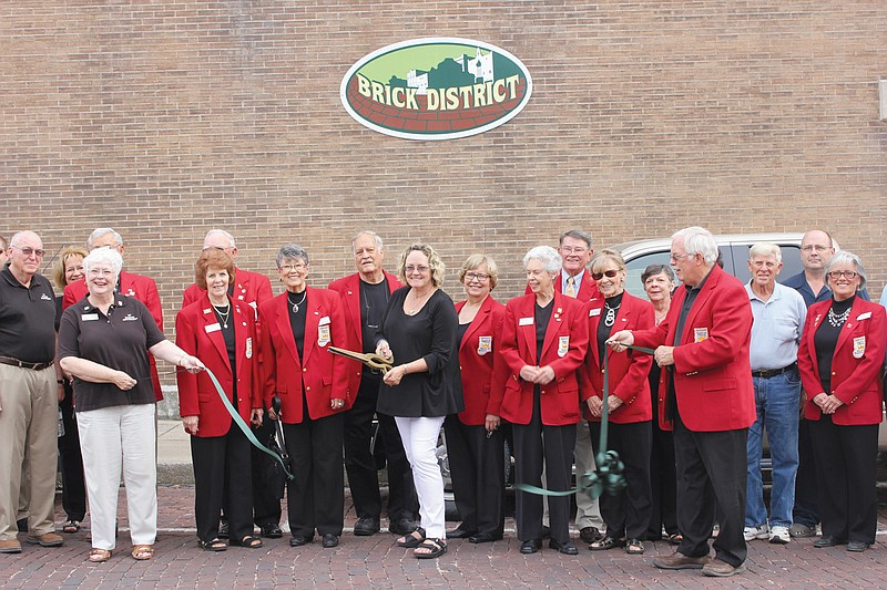 Flanked by Chamber Ambassadors, Court Street business owners and Fulton city officials, Smockingbirds owner Virginia McCoskrie snips the ribbon at a Kingdom of Callaway Chamber of Commerce event heralding the official kickoff of the Brick District.