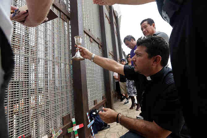 In this July 14, 2013 photo, Agustin Mendez, right, raises a chalice on the San Diego-side of the fence during a cross-border Sunday religious service. As federal lawmakers thousands of miles away consider further sealing the border, many here on the ground are trying to blur the line and unite a region that was split apart by the security crackdown since the Sept. 11 attacks. 