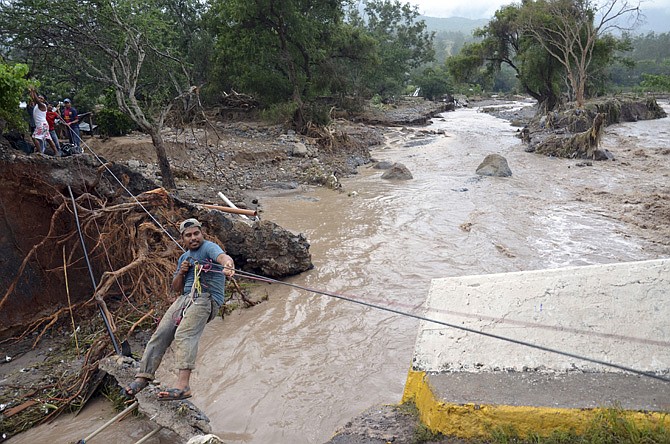 A man uses a makeshift zip line Wednesday to cross a river after a bridge collapsed under the force of the rains caused by Tropical Storm Manuel near the town of Petaquillas, Mexico. The death toll from devastating twin storms climbed to 97 on Thursday as isolated areas reported to the outside world.