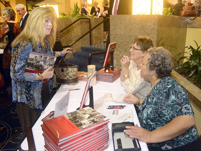 Pre-gala activites at the Capitol Plaza Hotel included a happy hour where dozens of guests mingled. Lois Hogan, left, purchases one of the Jefferson City Public Schools First 175 Years books from Suzanne Richter, middle and Saundra Allen, right.  