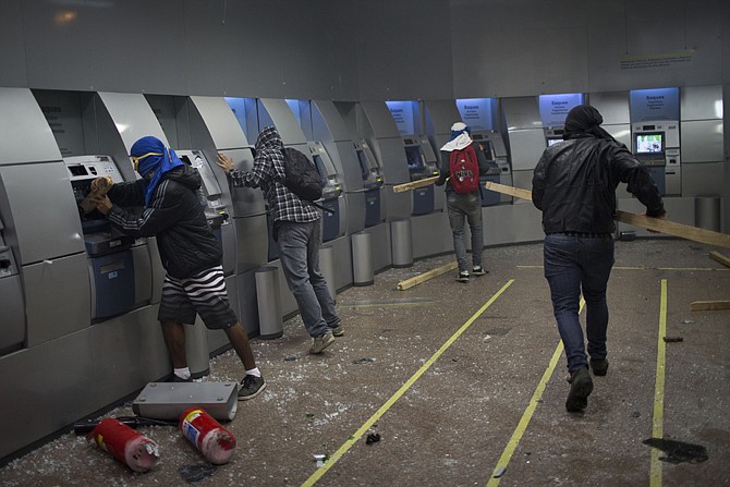 With their faces covered, demonstrators break ATM machines Monday inside a bank after a march in support of teachers on strike in Rio de Janeiro, Brazil. Teachers have been on strike demanding better pay for almost two months. 