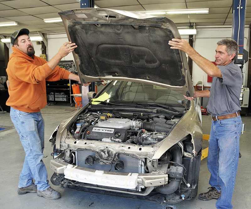 Auto body technicians Lance Wolters, left, and Rich Eichholz remove a damaged hood from a vehicle after it was brought to Kemna Collision Repair. The vehicle suffered damage in a collision with a deer. 