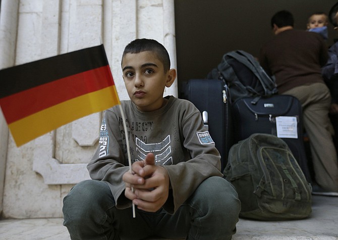 A Syrian refugee holds a German flag at the International Organization for Migration office as he waits with his family to board a bus to Beirut International Airport for a flight to Germany where they have been accepted for temporary resettlement.