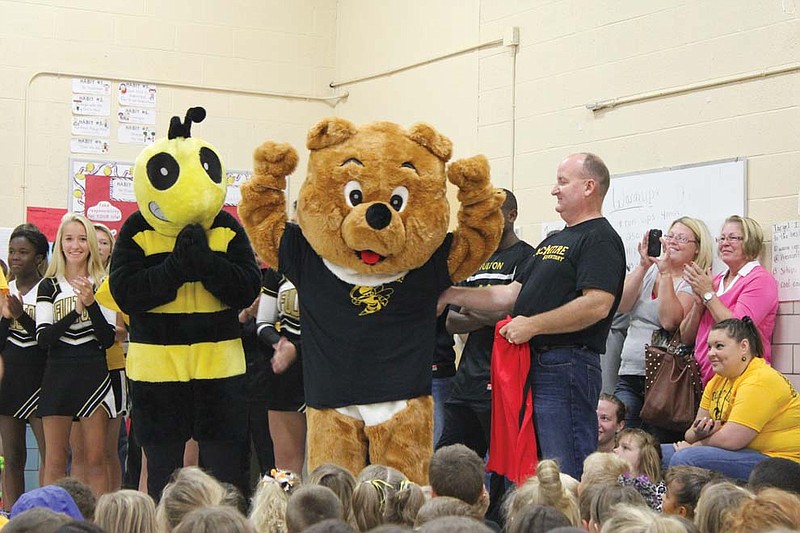 Harvey the Hornet helps Oscar the Bear show off his new Fulton Hornets T-shirt at a pep assembly Friday at McIntire Elementary School. Though McIntire will still use Oscar, the school changed its colors and mascot to black and gold abd the hornet to help foster solidarity and school spirit across the district.
