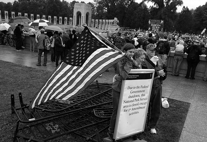 Kaylee Cantrell, left, 13, from Lexington Park, Md., with Sherry Cantrell and Michael Cantrell, both from Crossville, Tenn., pose for a photo in front of a sign and removed barricades at the World War II Memorial in Washington. A rally was organized to protest the closure of the Memorial and access to it by World War II veterans who traveled there on Honor Flight visits. 
