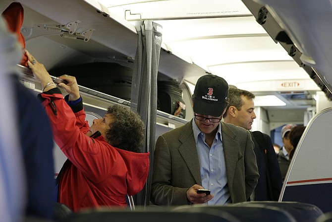A passenger checks his cellphone while boarding a flight Thursday in Boston. The Federal Aviation Administration issued new guidelines Thursday, under which passengers will be able to use devices to read, work, play games, watch movies and listen to music, from the time they board to the time they leave the plane.
