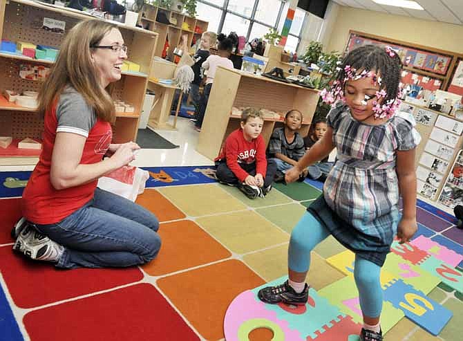 In a fun way to learn their numbers and to work on coordination skills, Samara Nyathanga, 5, plays hopscotch in her preschool classroom at Jefferson City's Southwest Early Childhood Center. At left is teacher, Jennifer Penserum, who works closely with the Title 1 students to help them improve their reading skills and numeral recognition skills.

