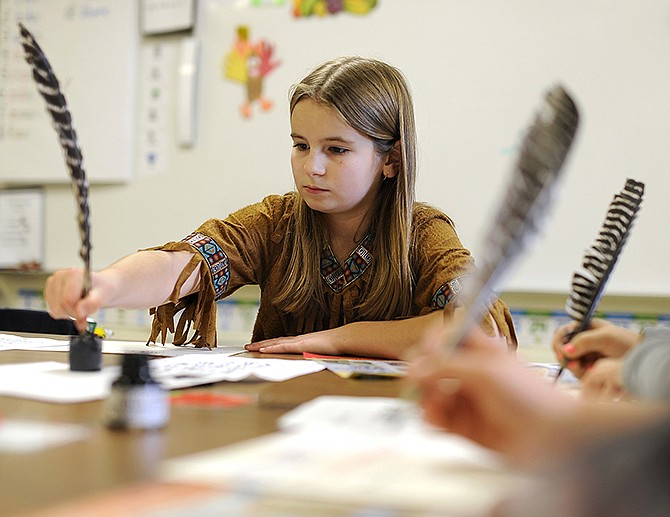 Fourth-grader Anna Hankins, at top, practices calligraphy Tuesday using a feather quill pen while dressed as a colonial-era Native American during Early American Day at Blair Oaks Elementary School.