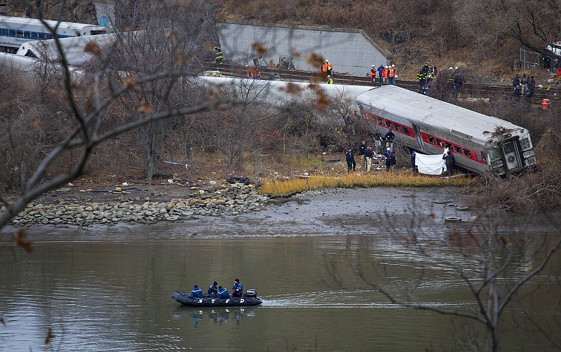 Viewed from Manhattan, first responders and others work near a victim next to a derailed Metro North passenger train in the Bronx borough of New York. The train derailed on a curved section of track coming to rest just inches from the water and causing multiple fatalities and dozens of injuries.