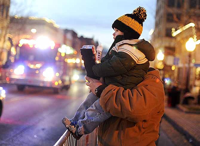 Oz Bruce rests against his dad Allan Bruce while holding on to his toy fire truck as the real thing makes its way up High Street during the annual Jefferson City Christmas Parade on Saturday.