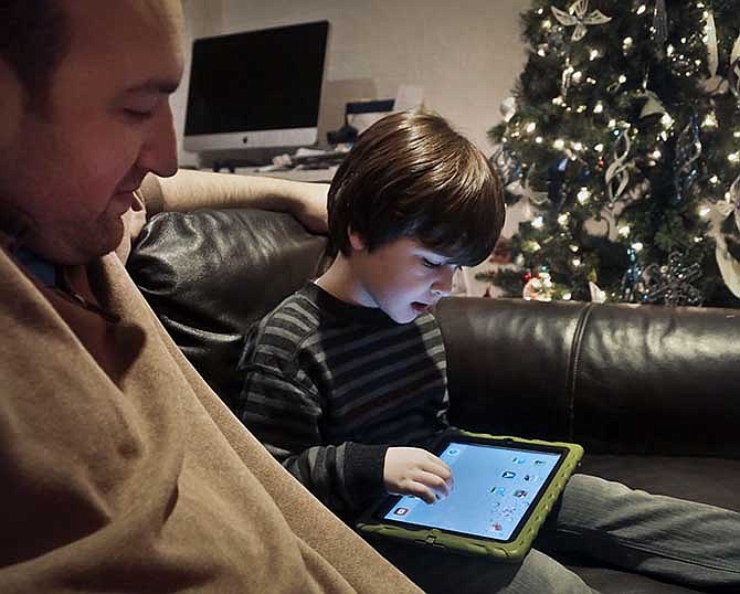 In this Dec. 3, 2013, photo, Adam Cohen looks as his son Marc, 5, uses a tablet at home in New York. Tablets of all types are expected to rank among the top holiday gifts for children this year, but some experts and advocates question the educational or developmental benefits for youngsters. 