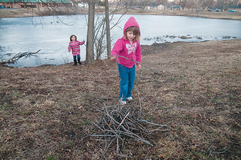 Alayna Thorpe, 4, tosses a stick into a pile of small branches on Thursday near Truman Lake in Fulton. Thorpe and her friend, seven-year-old Ava Miller, collected the sticks for a pretend fire. Thorpe's mother, Sara Berry of Fulton, said Thursday was the first time her daughter was out to play "in a while." The high for Fulton on Thursday was 44 degrees. The National Weather Service predicts the highs for Friday and Saturday to be 48 and 52 degrees, respectively, and the temperature will dip to 22 degrees on Sunday.