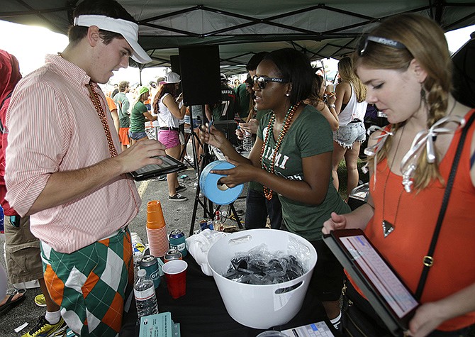 Miami student Mack Sokul, 18, left, fills out a survey at a tent set up by Generation Opportunity, a national conservative organization that targets young adults, while tailgating before the start of an NCAA college football game between Miami and Virginia Tech. It may have been the hottest tailgate party at the University of Miami's homecoming game, but the 100-yard stretch of free pizza and party tents, was also a carefully crafted strategy aimed at getting students to opt out of President Barack Obama's controversial new health law.