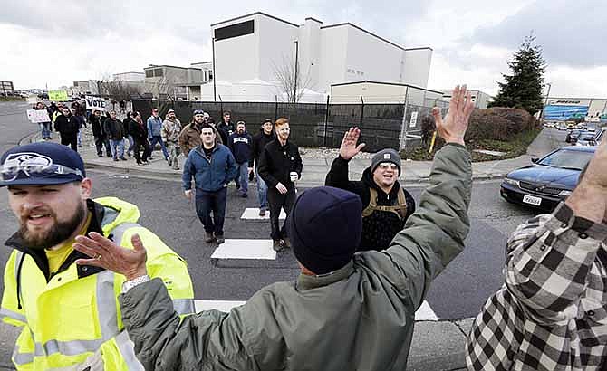 In this Dec. 18, 2013, file photo shows a small group of machinists union members are greeted by a supporter as they march away from a Boeing factory building toward the machinists' union hall in Everett, Wash. Boeing's contract proposal to machinists in the Puget Sound region would likely increase some workers' annual base salaries to more than $100,000 in the coming years. The contract offer going to a vote this week would slow the growth of machinists' wages starting in 2016, but workers would still get regular cost-of-living adjustments and an extra 1 percent pay increase every other year. 