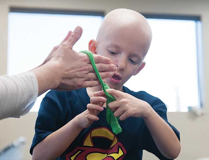 
Sam Santhuff, 5 of Fulton, wraps silly putty around the hands of physical therapist Kelly Nickelson at Atlas Physical Therapy in Fulton on Thursday. The exercise helps strengthen Santhuff's hands where neuropathy has developed as a result of chemotherapy.