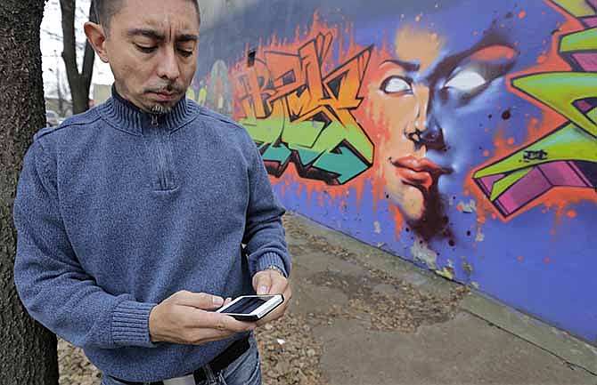 In this Dec. 6, 2013 photo, Eddie Bocanegra, co-executive director of the YMCA of Metropolitan Chicago's Youth Safety and Violence Prevention program, stands with his phone outside the organization's center in the Pilson neighborhood of Chicago. With the advent of social media usage by gangs, he says, "In the past you would have gangs approach you and say, 'Listen we're from the 'hood. Maybe you should get involved.' Now the kids are going to the gangs saying, 'I saw this. How can I be a part of it?'"