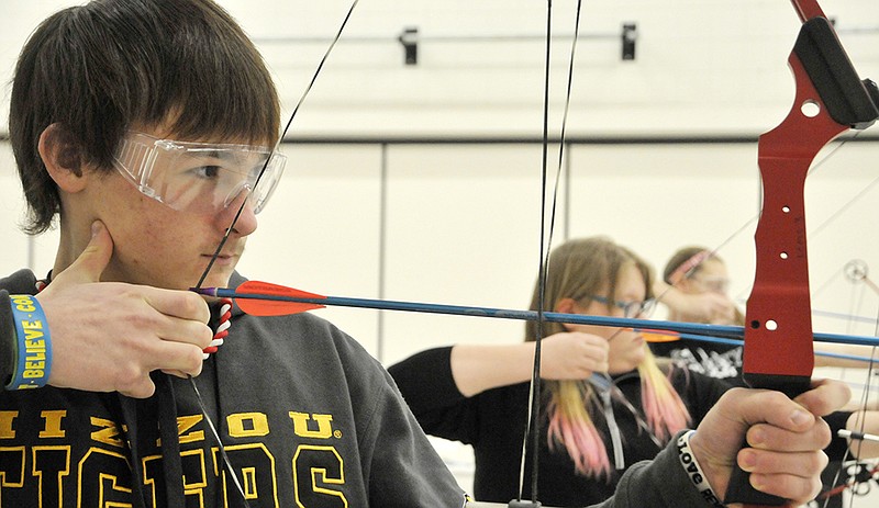 Harvey McNew pulls back on the bow string as he waits for the single whistle blast to indicate it's time to shoot the arrow. He is a student at Lewis & Clark Middle School and participates in "11 Steps to Archery Success" during Tuesday's P.E. class. Inset: Grace Christian draws back to place tension on the string before releasing the arrow as she uses the compound bow in physical education class at Lewis & Clark Middle School.