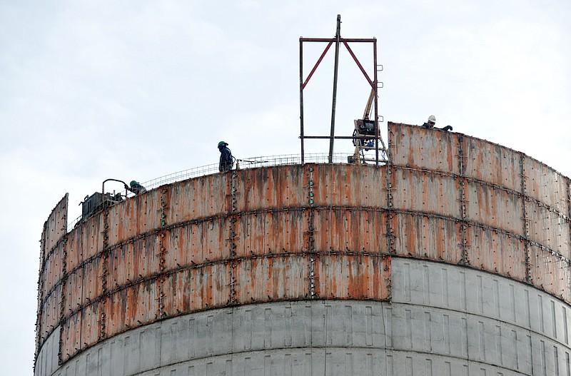 Workers from Caldwell Tanks of Louisville, Ky., stand 100 feet off the ground as they pour concrete and shake it down into the form of a 1.5-million gallon water holding tank adjacent to JCFD's new station 3 off Rock Hill Road on the city's west side. Inset below, a few dozen yards away, installers place siding on the south end of the new fire station. Contractors are waiting for a break in the weather so they can pour the concrete drive.