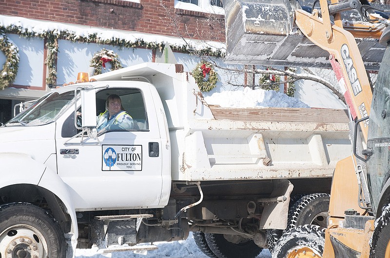 A city of Fulton employee looks over her shoulder as snow his dumped into the back of a truck. The trucks brought the snow to a baseball field off of Second Street. 