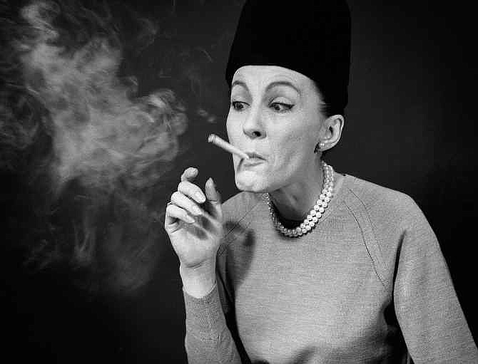 In this April 29, 1964 file photo, etiquette expert Cathy Bauby shows how puffing a cigarette like a steam engine shows that one is behind the "Jet Age" and doesn't care how one looks, during a demonstration in New York.