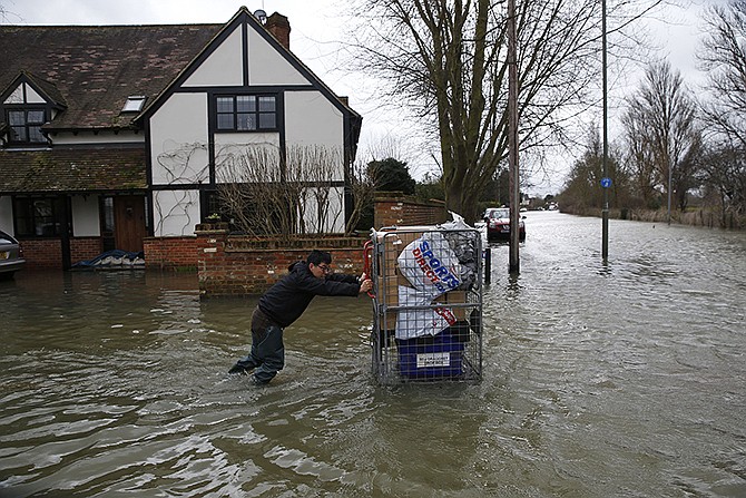 A local resident pushes belongings on a cart through the flooded part of the town of Staines-upon-Thames, England, as a police van patrols the area on Wednesday. Prime Minister David Cameron insisted Tuesday that money is no object in the battle against the widespread flooding that has engulfed parts of England.