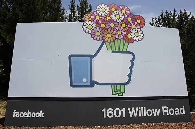 In this Sunday, May 13, 2012, file photo, flowers are added to a Facebook sign in front of Facebook headquarters in Menlo Park, Calif.