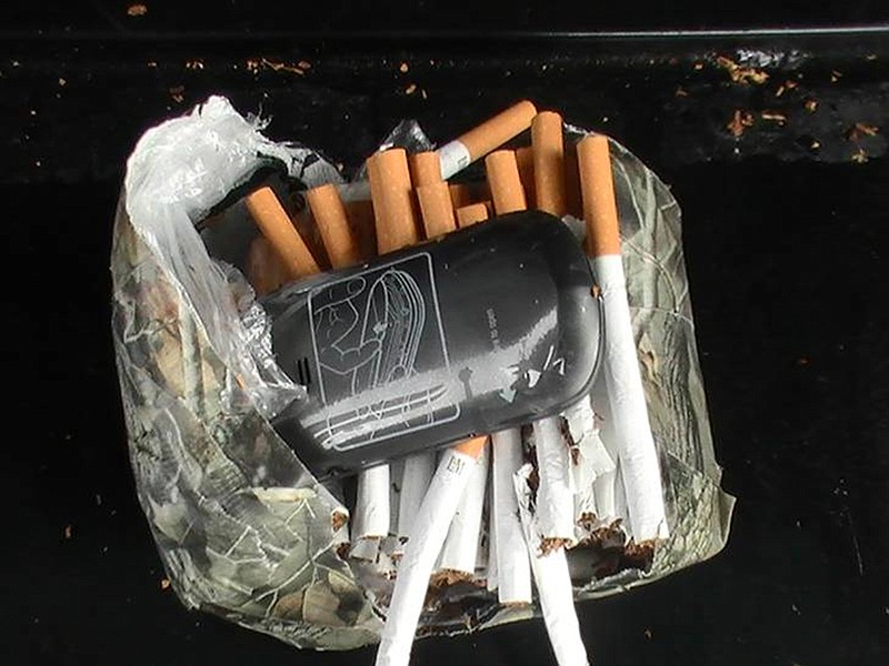 This undated photo provided by the Florida Department of Corrections shows a cellphone and cigarettes that were found inside a camouflage package near an undisclosed Florida state prison.