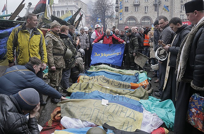 Activists and priests pay respects Thursday to protesters who were killed in clashes with police. A flag held by one activist reads "For Ukraine" in Kiev's Independence Square, the epicenter of the country's current unrest, in Kiev, Ukraine. Fierce clashes between police and protesters in Ukraine's capital have shattered the brief truce Thursday.