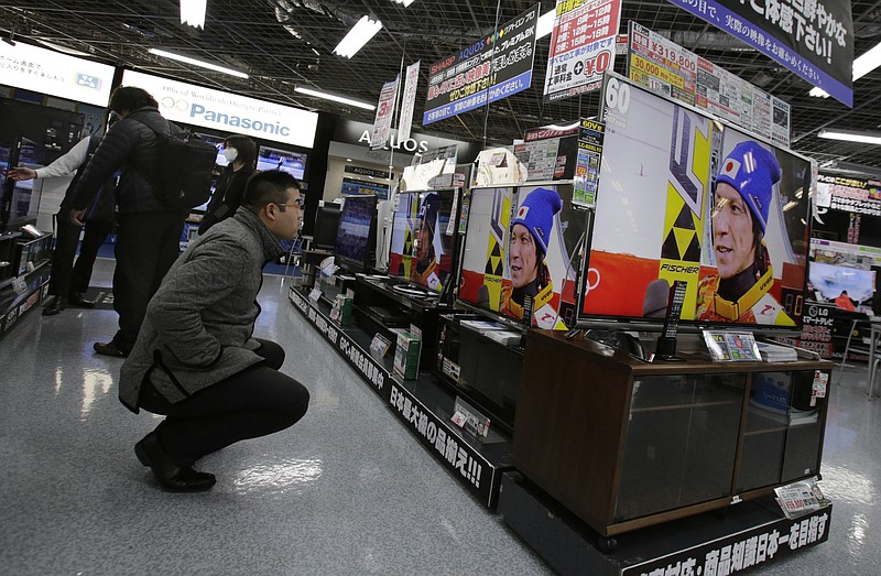 In this Wednesday, Feb. 19, 2014, photo, a shopper at an electronics store in Tokyo watches televisions showing recorded footage from an interview with Japanese ski jumper Noriaki Kasai, who won the silver medal in the large hill and the bronze in team ski jumping at the Sochi Olympics. The program is typical of the localized TV broadcasts in countries throughout the world during the Winter Olympics. 