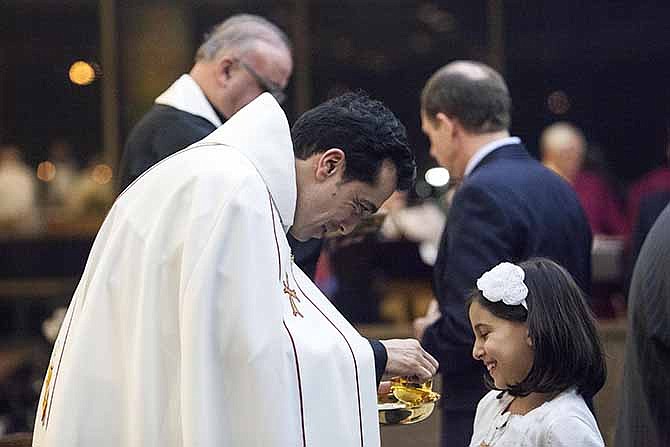 Wissam Akiki, who is married, left, serves his daughter, Perla, communion after being ordained during a ceremony at St. Raymond's Maronite Cathedral Thursday, Feb. 27, 2014, in St. Louis. Akiki is the first married priest to be ordained by the Maronite Catholic Church in the United States in nearly a century.