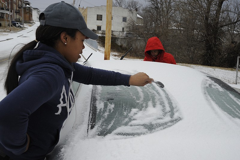 Emonis Sacus, front, helps her friend Shavontay Estes clean his car off Sunday afternoon on East High Street. After the roads were glazed with ice and snow Saturday night, many city residents apparently stayed inside on Sunday as there was little street traffic.
