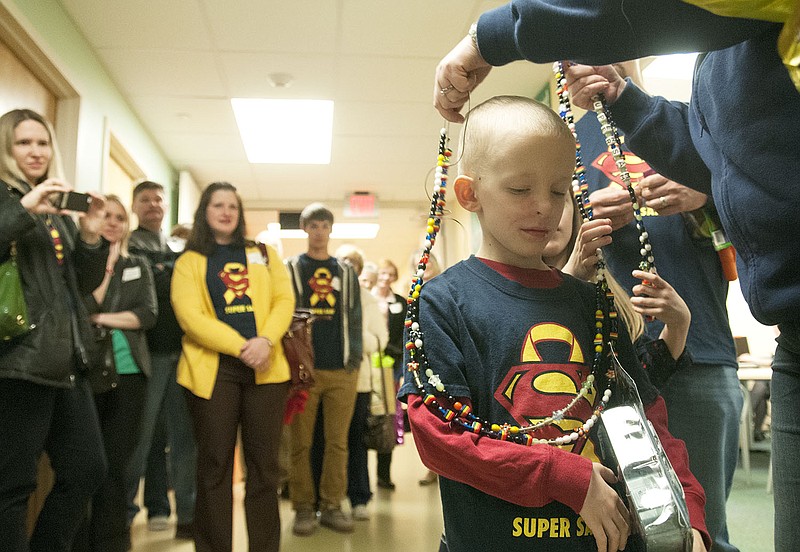 In this March 7, 2014 photo, Sam Santhuff's mother, Cassie Santhuff, places Sam's 13-and-a-half foot long strand of beads around his neck at St. Louis Children's Hospital among family and friends. The beads carry different meanings, each representing a moment in Sam's battle to beat cancer.