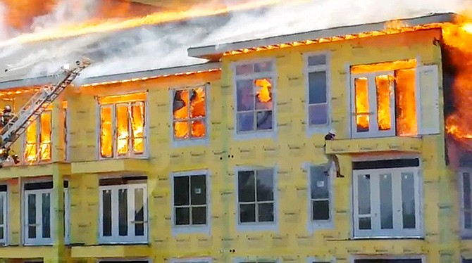 In this image taken from video provided by Karen Jones, Curtis Reissig lowers himself from a fifth floor balcony before swinging down to the one below as firefighters battle a five-alarm fire at a construction site Tuesday in Houston. 