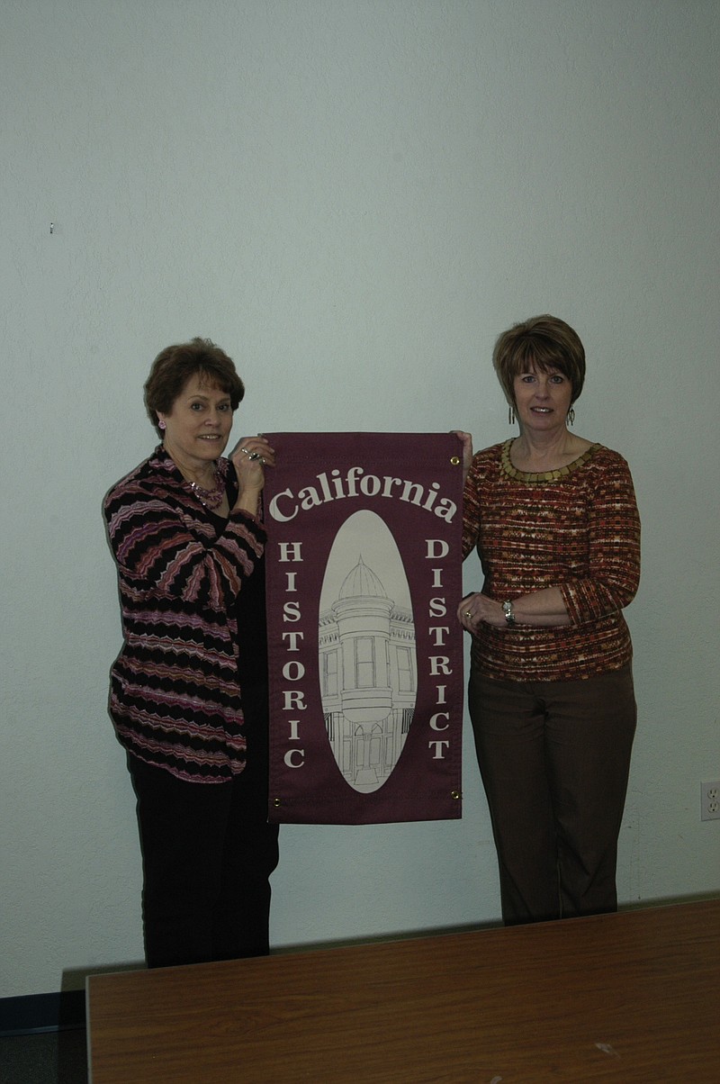 CPI Board member Beth Jungmeyer, left, and CHD Committee member Connie Walk, right, display one of the banners which will be placed on the period lights in the historic district.   