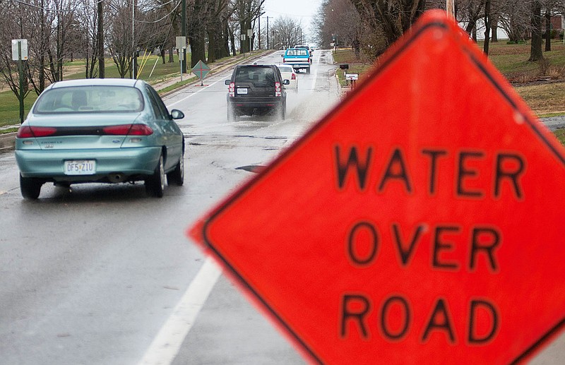 Drivers pass through a large puddle on Wood Street on Thursday after an morning thunderstorm. A Fulton City employee posted a "Water Over Road" sign to warn drivers to pass slowly over the puddle.