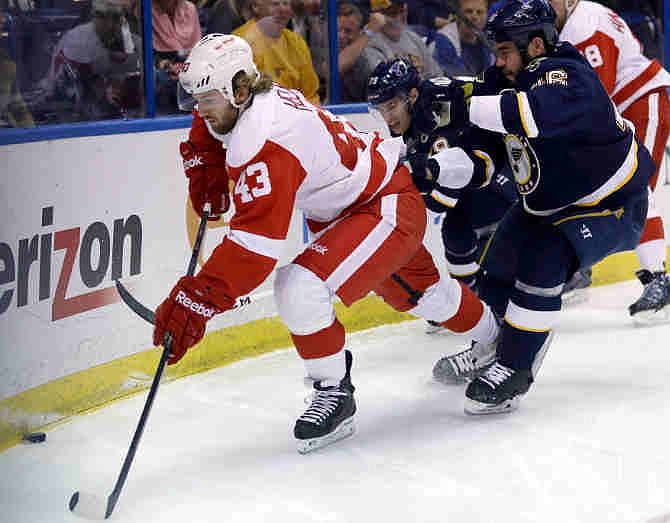 Detroit Red Wings' Darren Helm, left, reaches for a loose puck as St. Louis Blues' Adam Cracknell, center rear, and Roman Polak, of the Czech Republic, defend during the first period of an NHL hockey game Sunday, April 13, 2014, in St. Louis. 