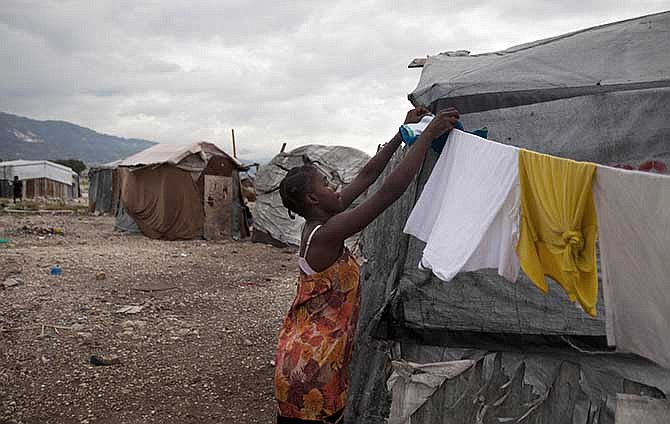  In this July 10, 2013 file photo, a woman fixes a clothes line next to her tent under cloudy skies caused by the nearby passing of Tropical Storm Chantal at the Jean-Marie Vincent camp for people displaced by the 2010 earthquake in Port-au-Prince, Haiti. A study released on Monday, April 7, 2014 finds that many of the camps are growing again, even as the overall population of quake refugees is falling. The study from the International Organization for Migration attributes the phenomenon mostly to people who have returned because they can't afford rents elsewhere.