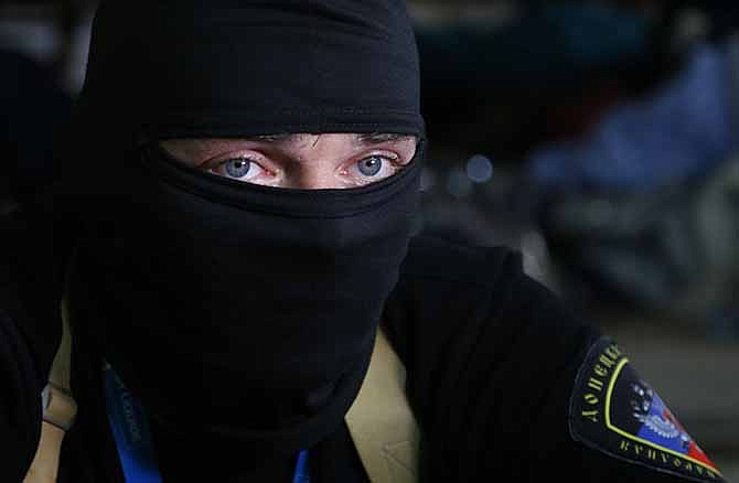 A masked pro-Russian activist guard looks through a window of the regional administration building seized earlier in Donetsk, Ukraine, Friday, April 18, 2014. Pro-Russian insurgents in Ukraine's east who have been occupying government buildings in more than 10 cities said Friday they will only leave them if the interim government in Kiev resigns.