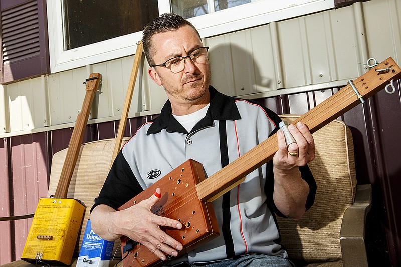 Ashland resident Travis Naughton plays a homemade cigar box guitar at his house last week. Naughton makes primitive instruments from recycled items as an ode to simpler times when you used what you had in order to make music. Inset below. Naughton plays his washtub bass.