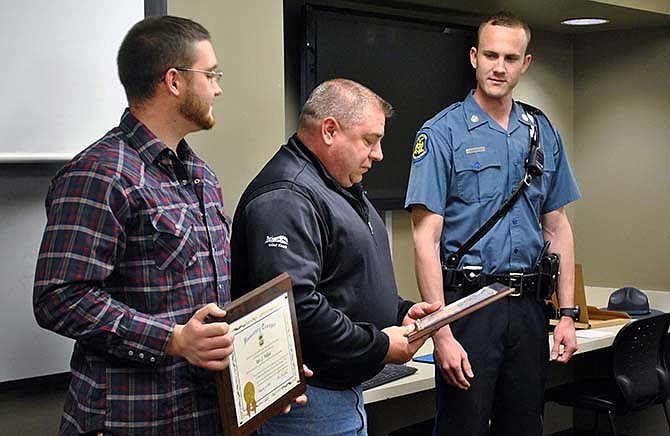 Richard Miller, center, looks at his Honorary Trooper award, Friday, alongside his son, Ian, left, who received the same award for lifesaving efforts they performed for two occupants involved in a vehicle crash Jan. 1 near their Camden County home. Missouri Highway Patrol Trooper Kyle A. Schrage, who investigated the incident, presented the two men the awards Friday at the Camden County Sheriff's Department in Camdenton. 